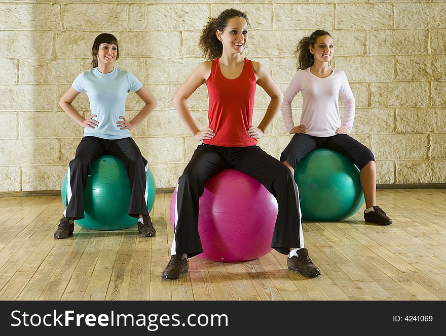 A group of women making exercise sitting on big balls and holding hands on hips. Front view. A group of women making exercise sitting on big balls and holding hands on hips. Front view.