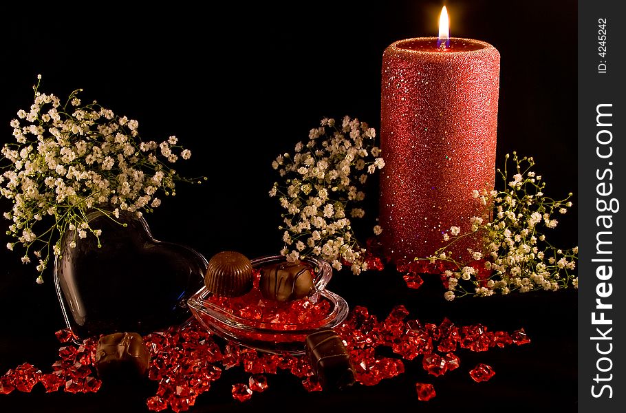 A red rose bud on a black background with red beads lying around. A red rose bud on a black background with red beads lying around