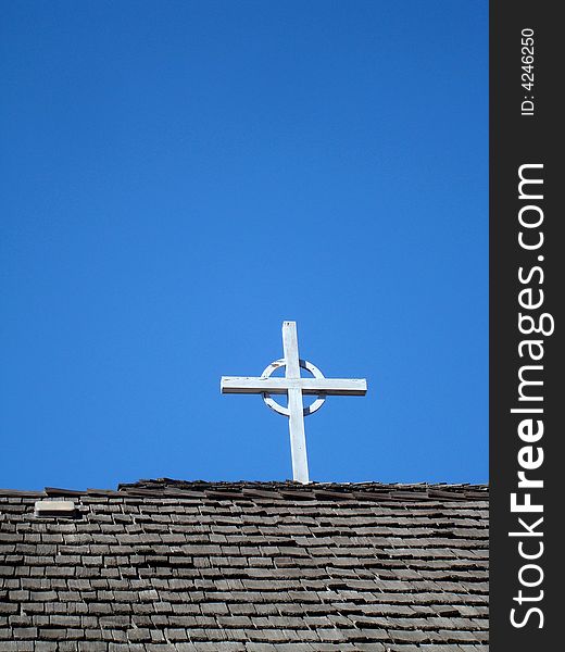 Cross on church roof with blue sky behind.