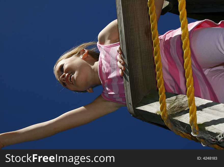 Pretty white caucasian girl playing on a climber on a hot day with blue sky in the background. Pretty white caucasian girl playing on a climber on a hot day with blue sky in the background