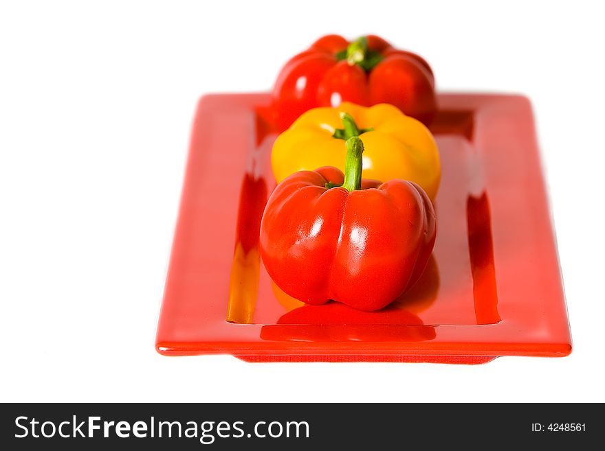 Red and yellow bellpeppers on a red serving plate, isolated on a white background. Red and yellow bellpeppers on a red serving plate, isolated on a white background.