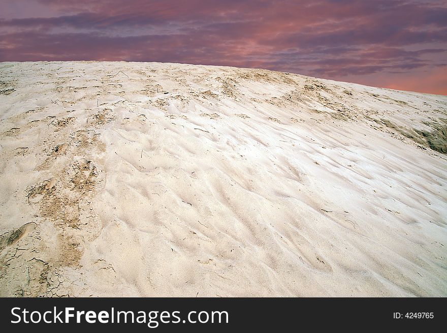 Single pale yellow sand dune with shoe tracks. Sunrise.