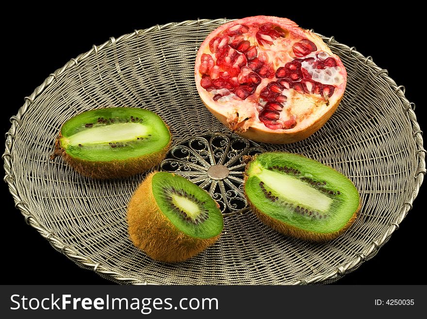 Kivi and pomegranate on a wattled metal tray on a black background. Kivi and pomegranate on a wattled metal tray on a black background