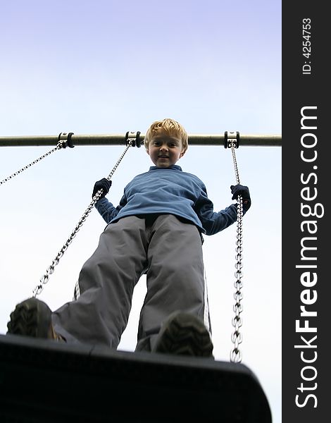 A young boy standing on a swing viewed from below