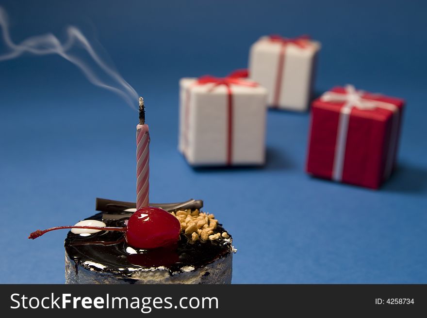 Chocolate cake with candle and gift boxes on blue background. Dessert series. Chocolate cake with candle and gift boxes on blue background. Dessert series.