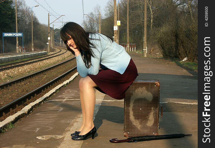 Young girl waiting for the train on the empty railway platform with an old suitcase