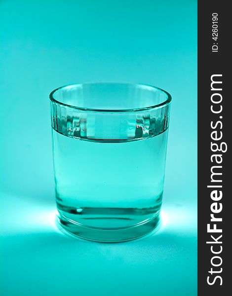 Single glass of water in blue-green colour macro