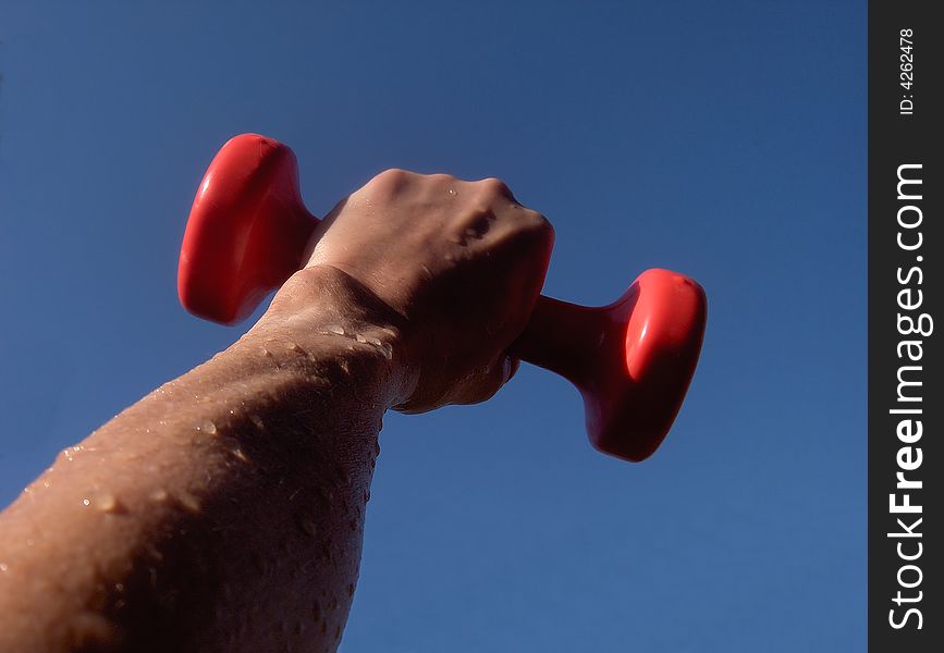 Arm and fist holding dumbbell against the sky. Arm and fist holding dumbbell against the sky