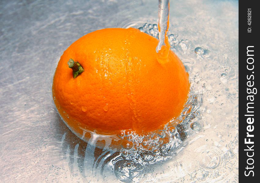 Orange under a jet of water on a metal surface. Orange under a jet of water on a metal surface.