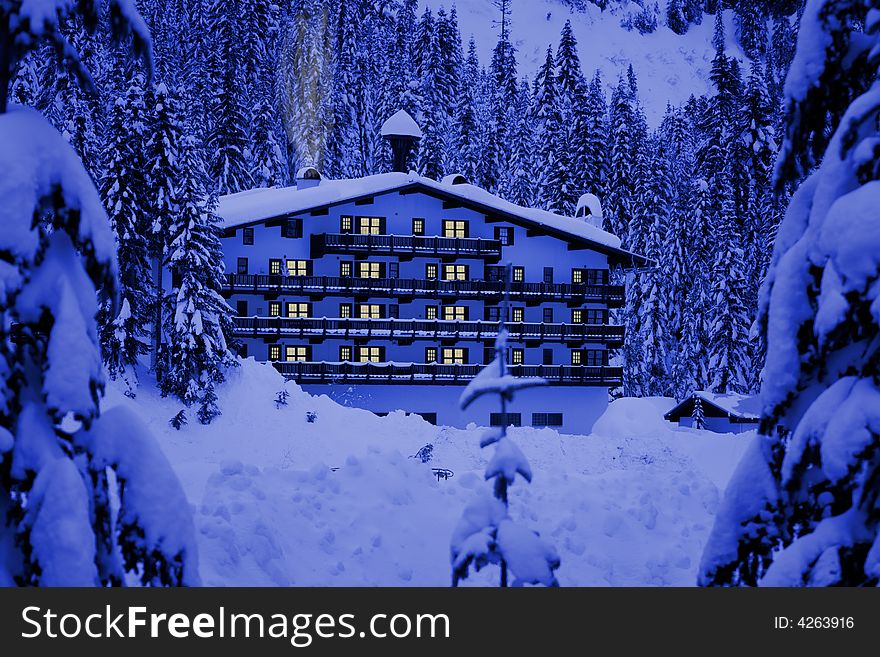 A hotel located in mountains covered by deep snow. Glow of windows and smoke give warm and cozy holiday feeling. A hotel located in mountains covered by deep snow. Glow of windows and smoke give warm and cozy holiday feeling.