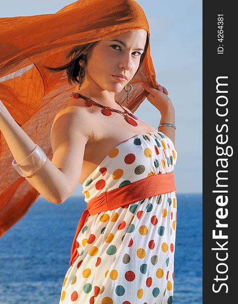 Fashion model holding oragne cloth against ocean background. Fashion model holding oragne cloth against ocean background