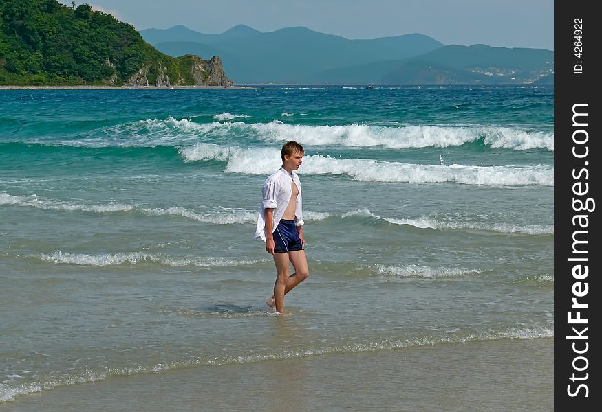 A boy at sea. On background are whire surf and green cape. Russian Far East, Primorye, Japanese Sea. A boy at sea. On background are whire surf and green cape. Russian Far East, Primorye, Japanese Sea.