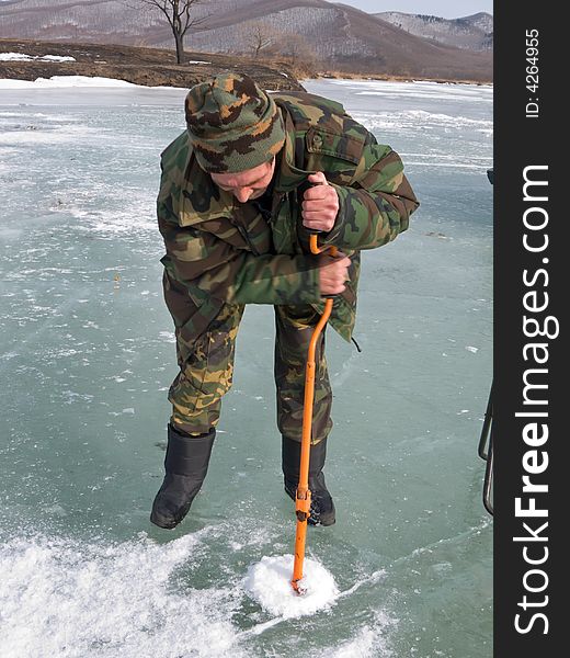 A winter fishing on river. People is fishing the smelt. A man drills a hole in ice. Russian Far East, Primorye, Kievka river. A winter fishing on river. People is fishing the smelt. A man drills a hole in ice. Russian Far East, Primorye, Kievka river.