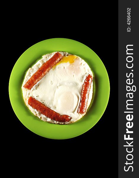 Eggs and sausages on a green plate, isolated on black. Eggs and sausages on a green plate, isolated on black