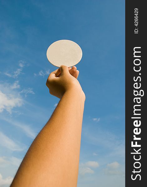 Arm holding circular white space against a blue partly cloudy sky. Arm holding circular white space against a blue partly cloudy sky