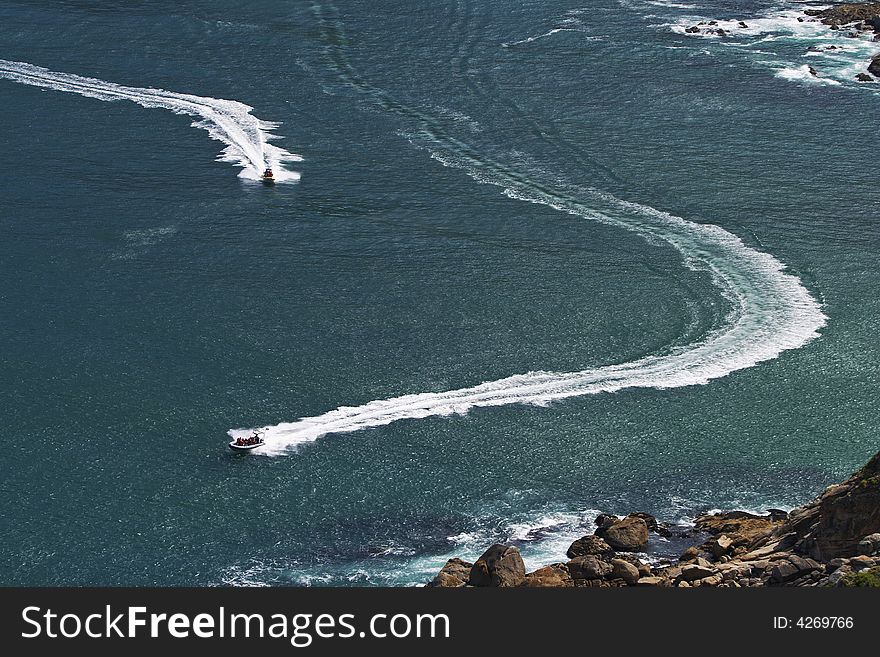 Two ski boats carrying tourists on a joy ride trace patterns with their wakes across the waters of Hout Bay, Cape Town. Two ski boats carrying tourists on a joy ride trace patterns with their wakes across the waters of Hout Bay, Cape Town.