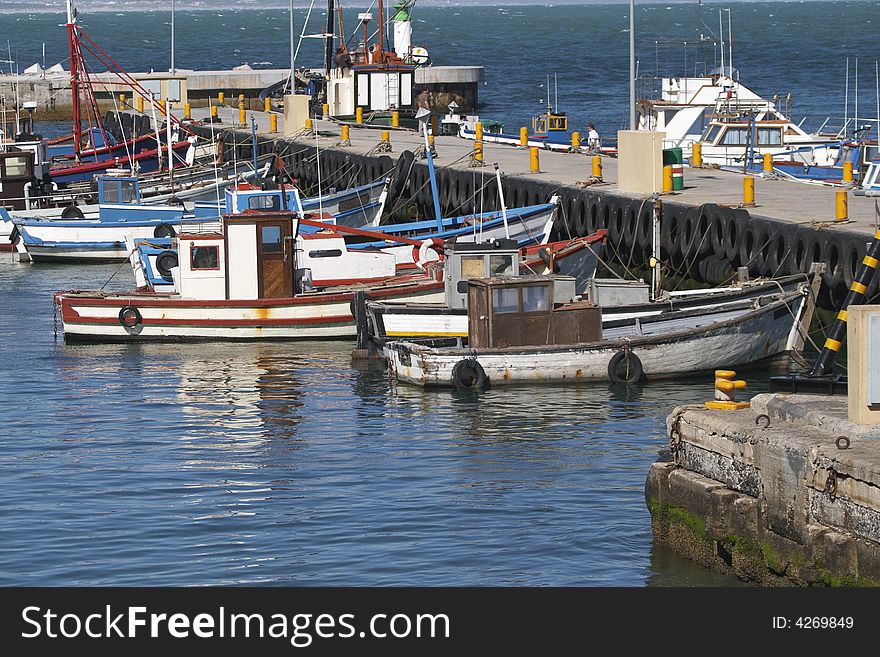 Fishing boats moored to the pier in Kalk Bay harbour, Cape Town, South Africa. The colourful boats are brightly reflected in the water of the harbour. Fishing boats moored to the pier in Kalk Bay harbour, Cape Town, South Africa. The colourful boats are brightly reflected in the water of the harbour.