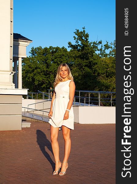 Young woman in white dress posing standing in a park at sunset