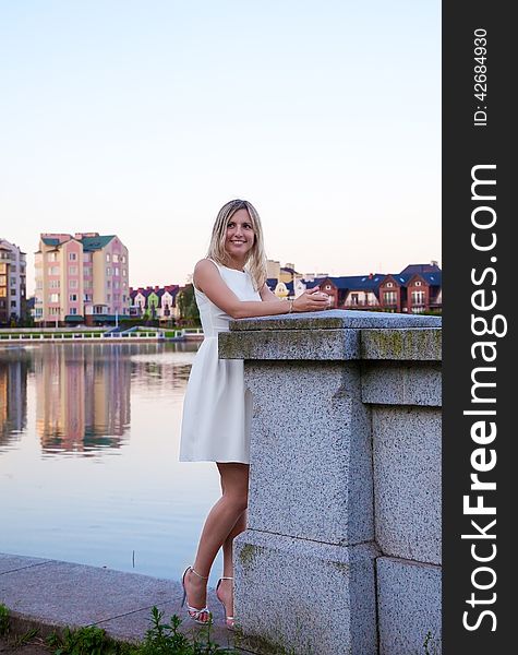 Beautiful woman in a white dress standing on the waterfront at sunset
