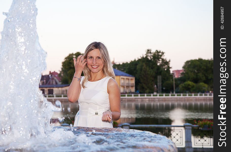 Young beautiful woman in a white dress near the fountain at sunset