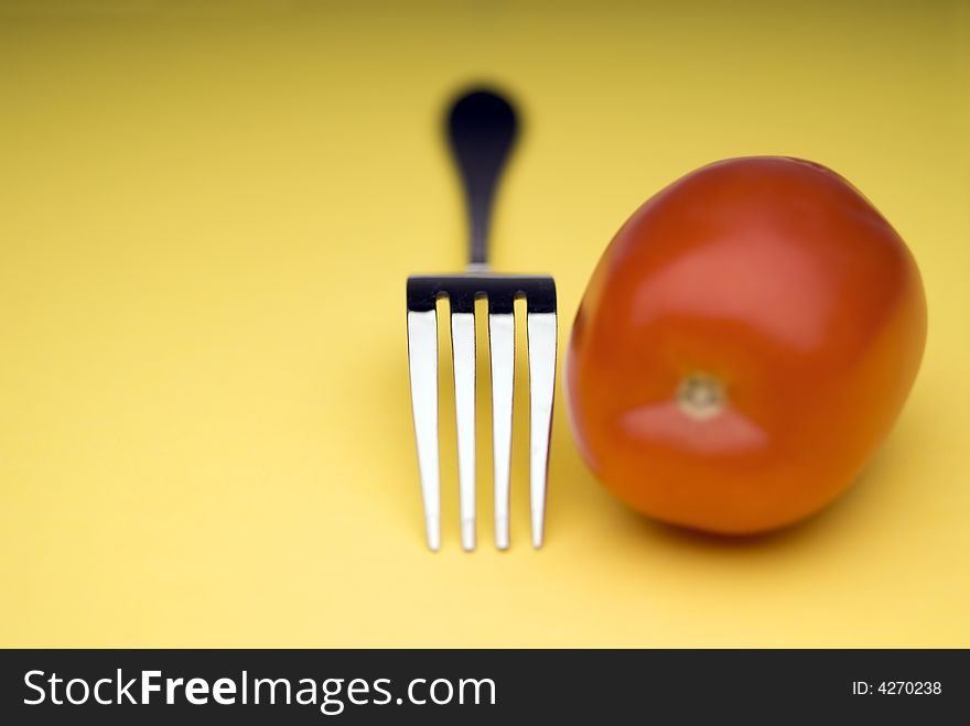 Snappy image of a fork and a tomato on a bright yellow background. Snappy image of a fork and a tomato on a bright yellow background