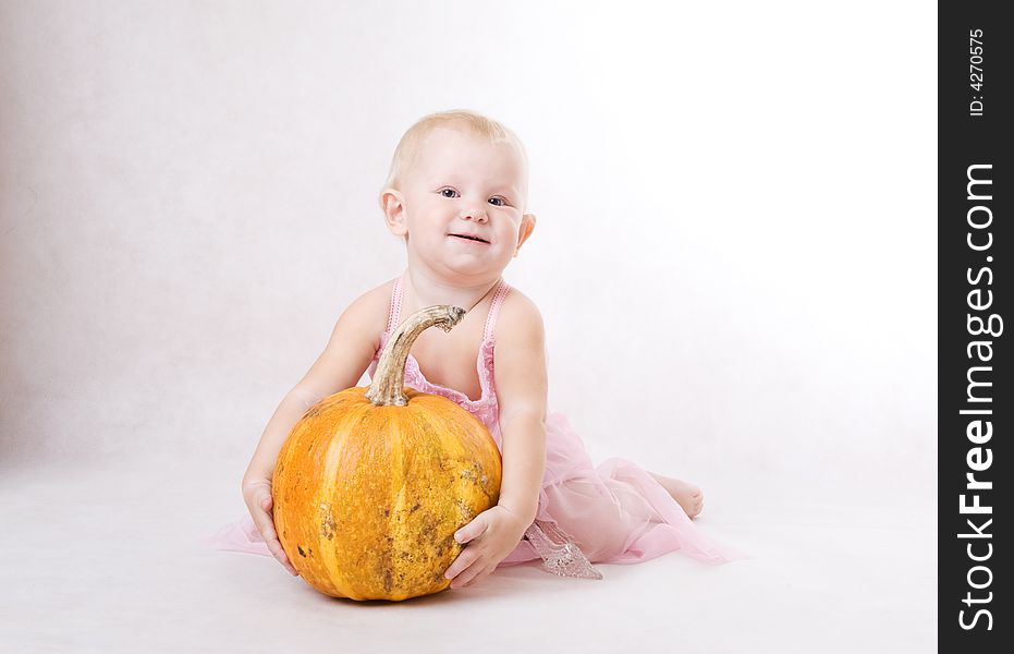 A smiling little girl embraces a pumpkin and a crystal shoe near by