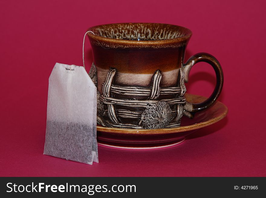 It is a an interesting cup with a tea bag on a red background. It is a an interesting cup with a tea bag on a red background