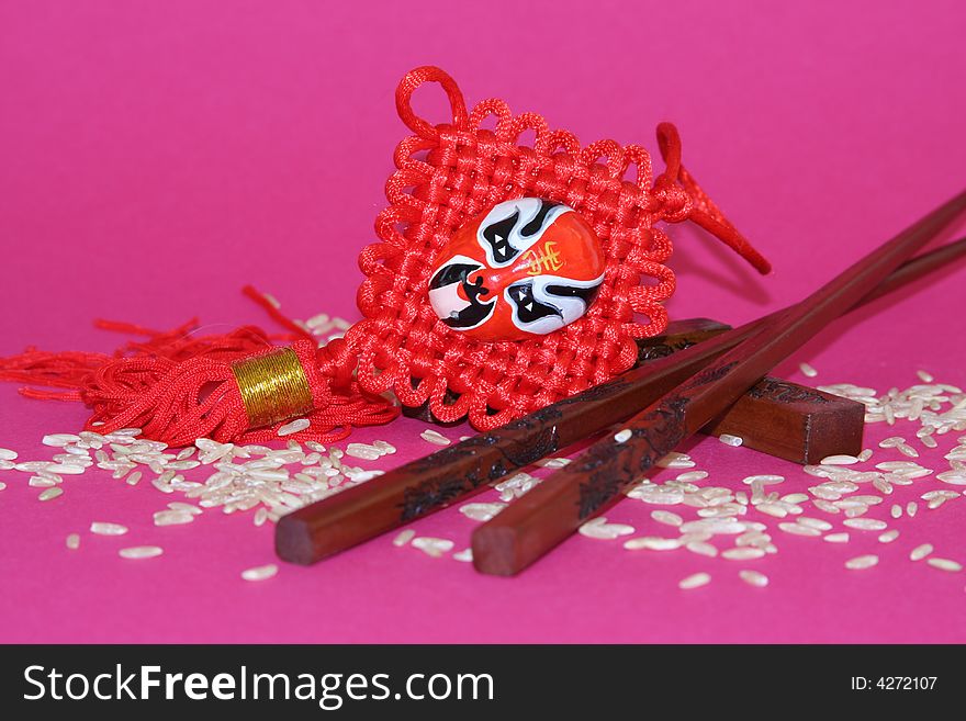 It is a Chinese traditional objects for food and decoration plus rice on a pink background. It is a Chinese traditional objects for food and decoration plus rice on a pink background