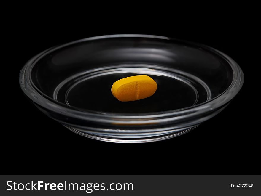 Yellow pill in bright glass saucer