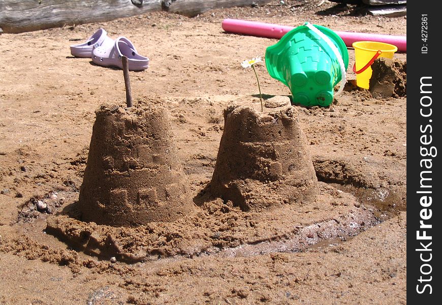 Sandcastle in the foreground with beach toys and shoes in background. Sandcastle in the foreground with beach toys and shoes in background