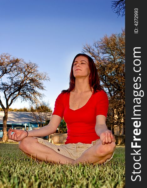 A woman meditates during relaxing afternoon in a sunny park, framed against a deep blue sky. A woman meditates during relaxing afternoon in a sunny park, framed against a deep blue sky.