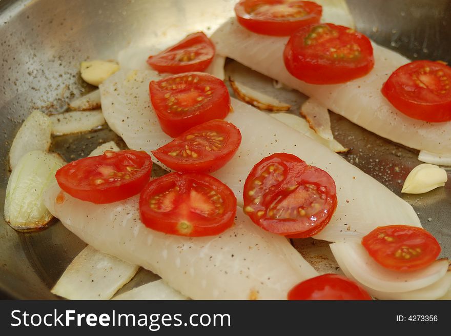 Three fish fillets in a frying pan with onions and tomatoes. Three fish fillets in a frying pan with onions and tomatoes