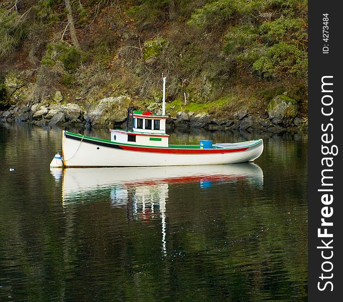 Clean, vibrant boat anchored in calm bay waters. Rock, bushes, and trees serve as the background. Clean, vibrant boat anchored in calm bay waters. Rock, bushes, and trees serve as the background.