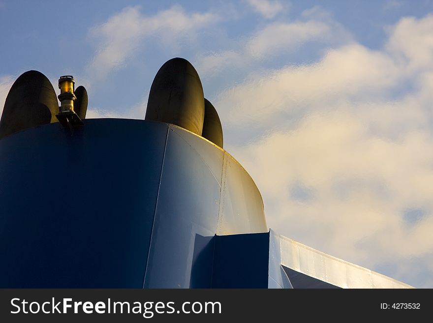 The tip of a blue ferry boat chimney stack. The background is filled with a blue sky with white clouds. Heat above the chimney creating a heat wave distortion effect in part of the clouds' image. The tip of a blue ferry boat chimney stack. The background is filled with a blue sky with white clouds. Heat above the chimney creating a heat wave distortion effect in part of the clouds' image.