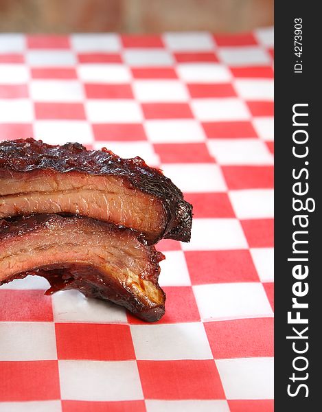 Babyback spare barbeque pork ribs on a checkered restaurant tissue room for text. Babyback spare barbeque pork ribs on a checkered restaurant tissue room for text