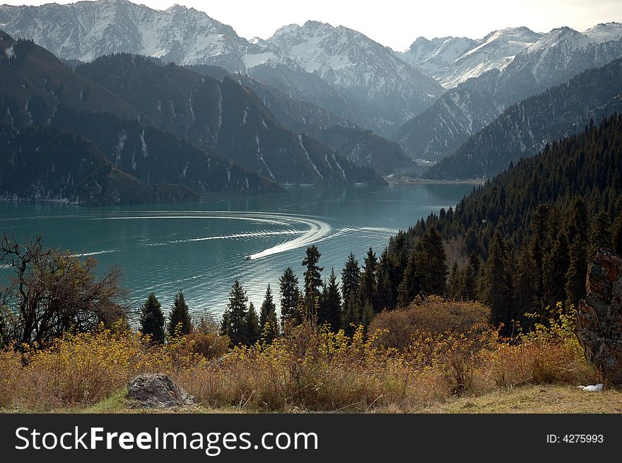 The mountain is around the lake, one yacht is passing by the surface of lake. The mountain is around the lake, one yacht is passing by the surface of lake.