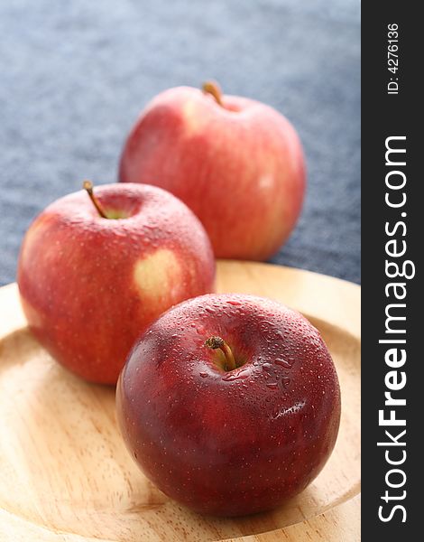 Red apples with drops of water on wooden plate with blue denim background. Red apples with drops of water on wooden plate with blue denim background