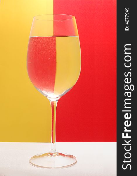 Glass of water on the background divided by yellow and red colour. Glass of water on the background divided by yellow and red colour