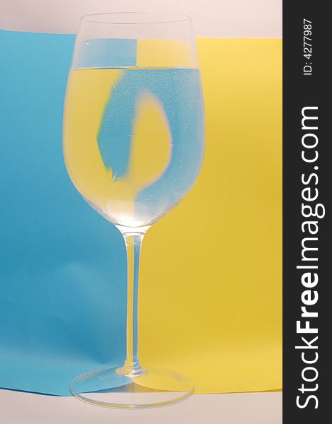 Glass of water on the background divided by yellow and blue colour. Glass of water on the background divided by yellow and blue colour