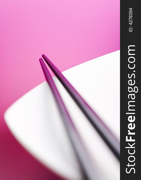Chopsticks on the white plate over pink background