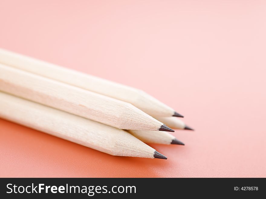 Pile of wooden pencils over a light red background. Pile of wooden pencils over a light red background