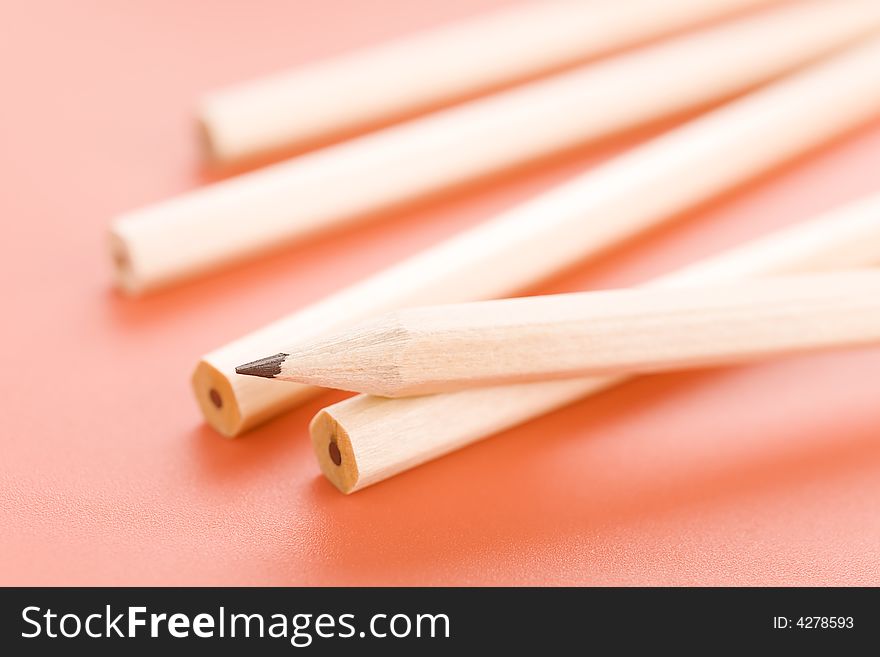 Pile of wooden pencils over a light red background. Pile of wooden pencils over a light red background