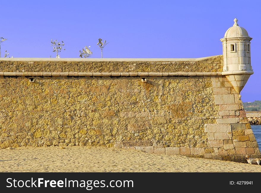 Portugal, area of Algarve, Lagos: typical architecture. Blue sky and yellow stone fortress; detail of one tower. Portugal, area of Algarve, Lagos: typical architecture. Blue sky and yellow stone fortress; detail of one tower