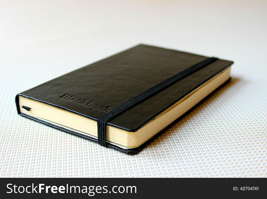 A closed black book lying on a white flooring.