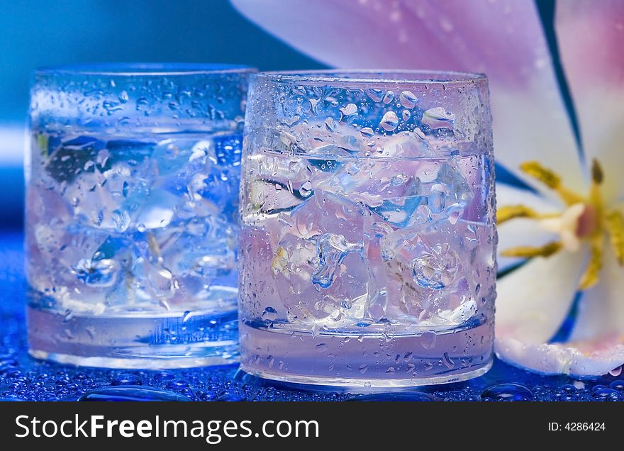 Glasses with water and flower over blue