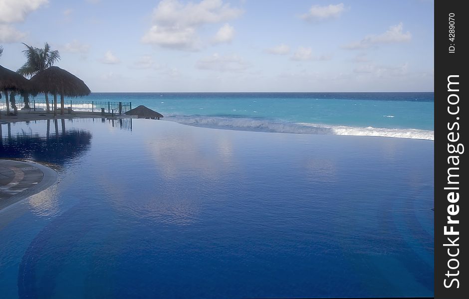 A blue lagoon type pool at a resort with ocean and clouds in background. A blue lagoon type pool at a resort with ocean and clouds in background