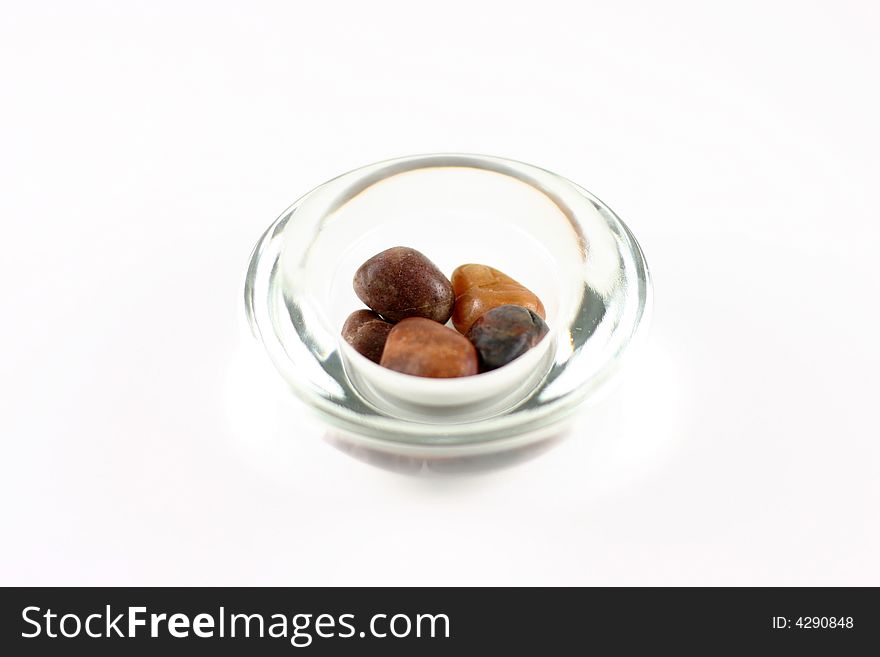 Warm colored rocks in a simple glass bowl. Exposure creates a blown out look. White background. Warm colored rocks in a simple glass bowl. Exposure creates a blown out look. White background