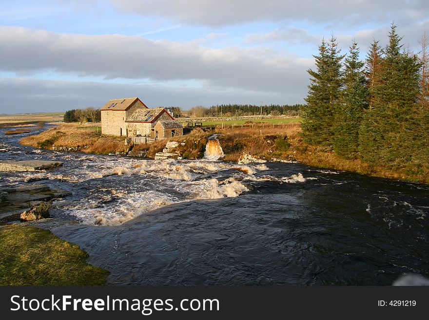 An old mill, a flooding mill race and a river in a stunning landscape with trees. An old mill, a flooding mill race and a river in a stunning landscape with trees