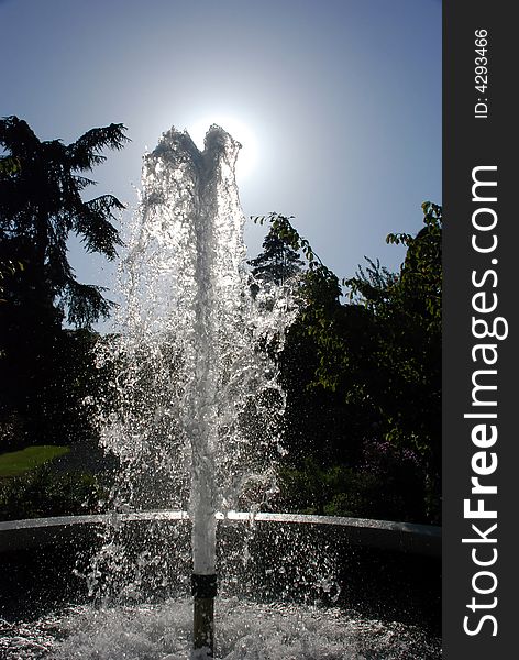 Water fountain in the garden against the sun and blue sky