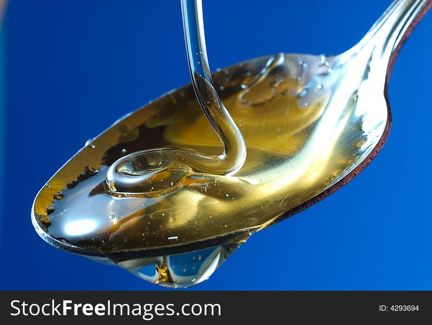 Honey pouring into a spoon on blue background. Honey pouring into a spoon on blue background.